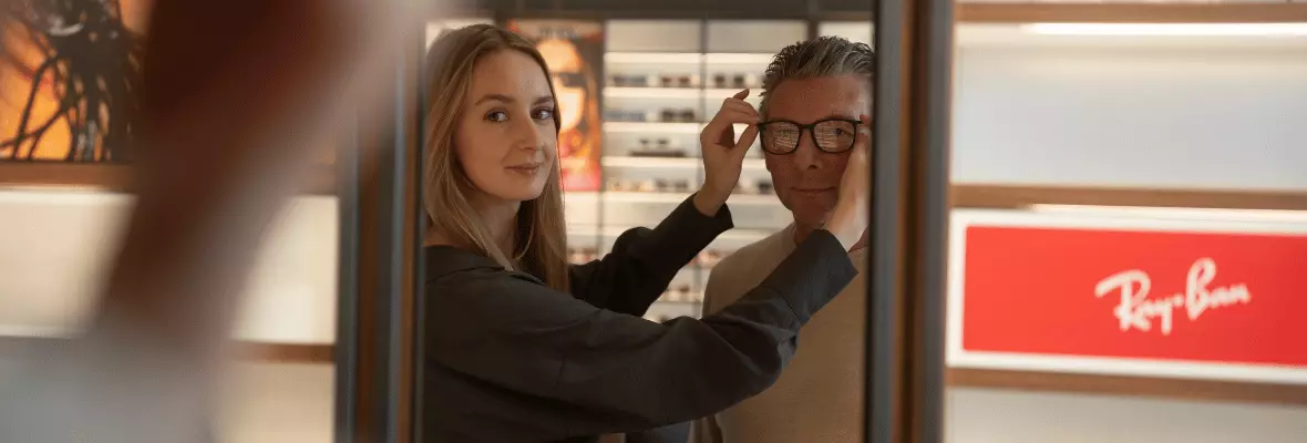 Pearle verkoopmedewerker Karlien past montuur bij een klant  Klant kijkt in de spiegel naar een doorzichtig montuur